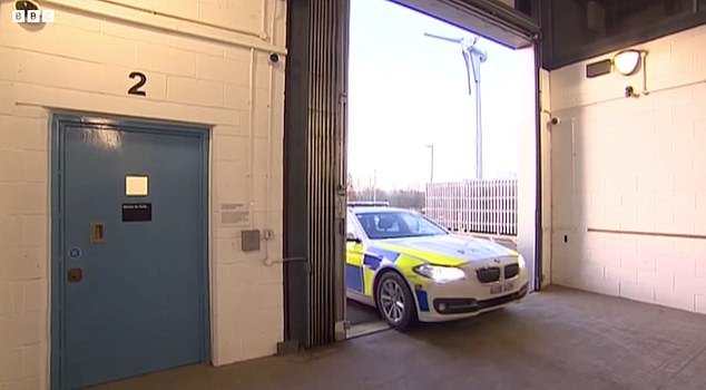 The clip begins with a police car being driven into the station through a large security gate