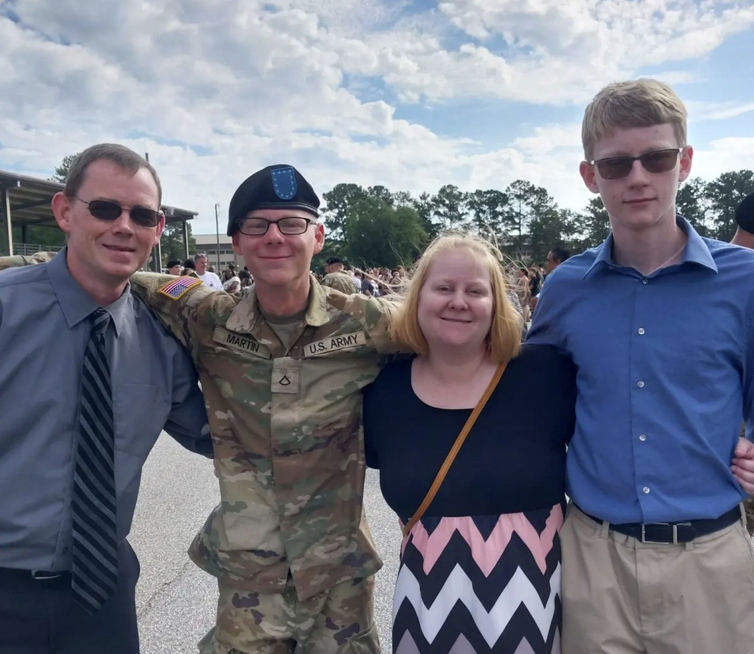 A soldier in uniform smiles with family members during a military event, showcasing a moment of pride and celebration.