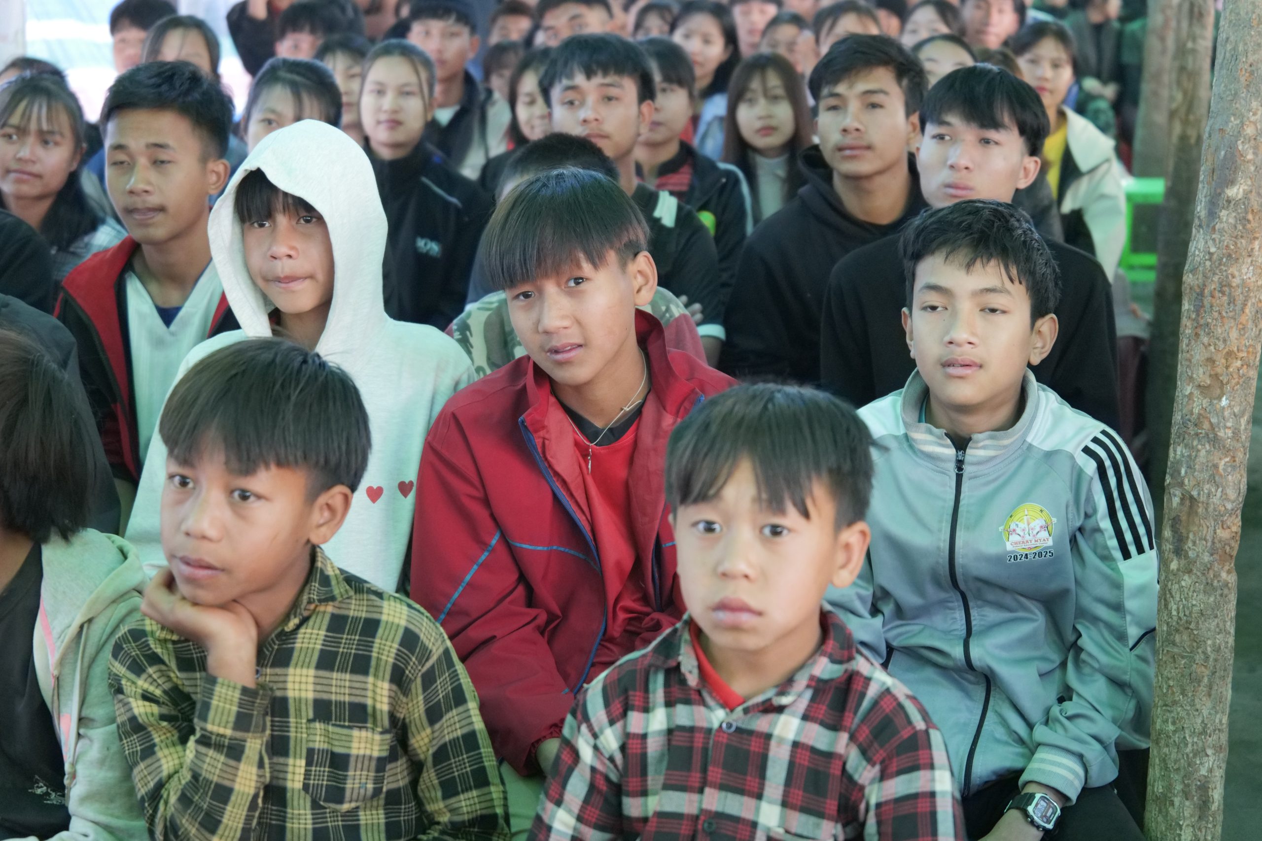 Group of diverse young students attentively listening during a classroom session, showcasing engaged expressions and varied clothing styles.