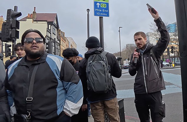A male clutching a microphone and Bible (right) can be heard preaching the Gospel in Whitechapel Road, just yards from the East London Mosque