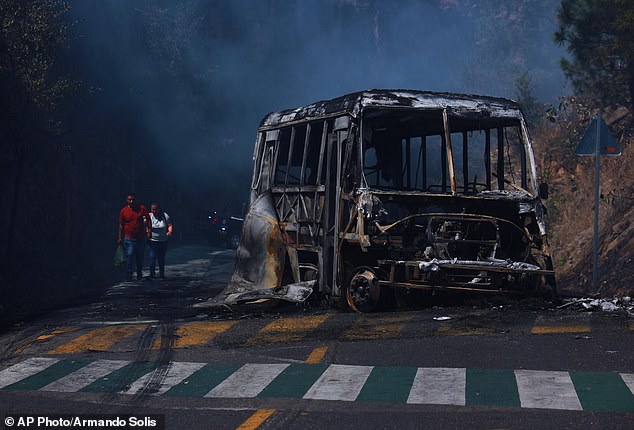 Pedestrians walk past a charred vehicle after it was set on fire, on a road in Cointzio, Michoacán state, Mexico on Sunday