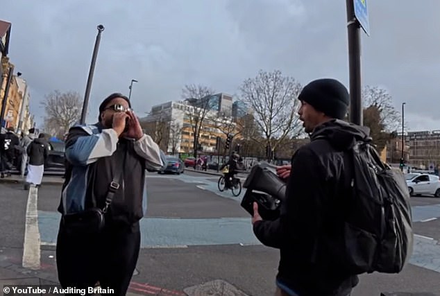 The man wearing sunglasses and a black, blue, and white tracksuit top repeatedly bellows the derogatory remark