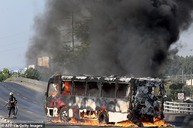 A firefighter extinguishes a burning bus set on fire by organised crime groups