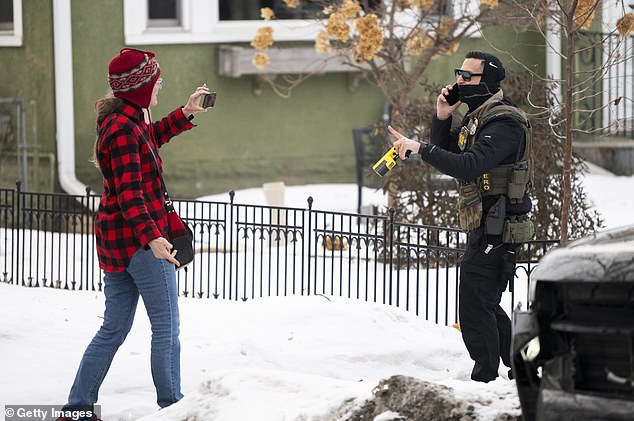An ICE agent holding a taser points at a woman holding a phone after one of their vehicles got a flat tire on Penn Avenue on February 5, 2026 in Minneapolis, Minnesota