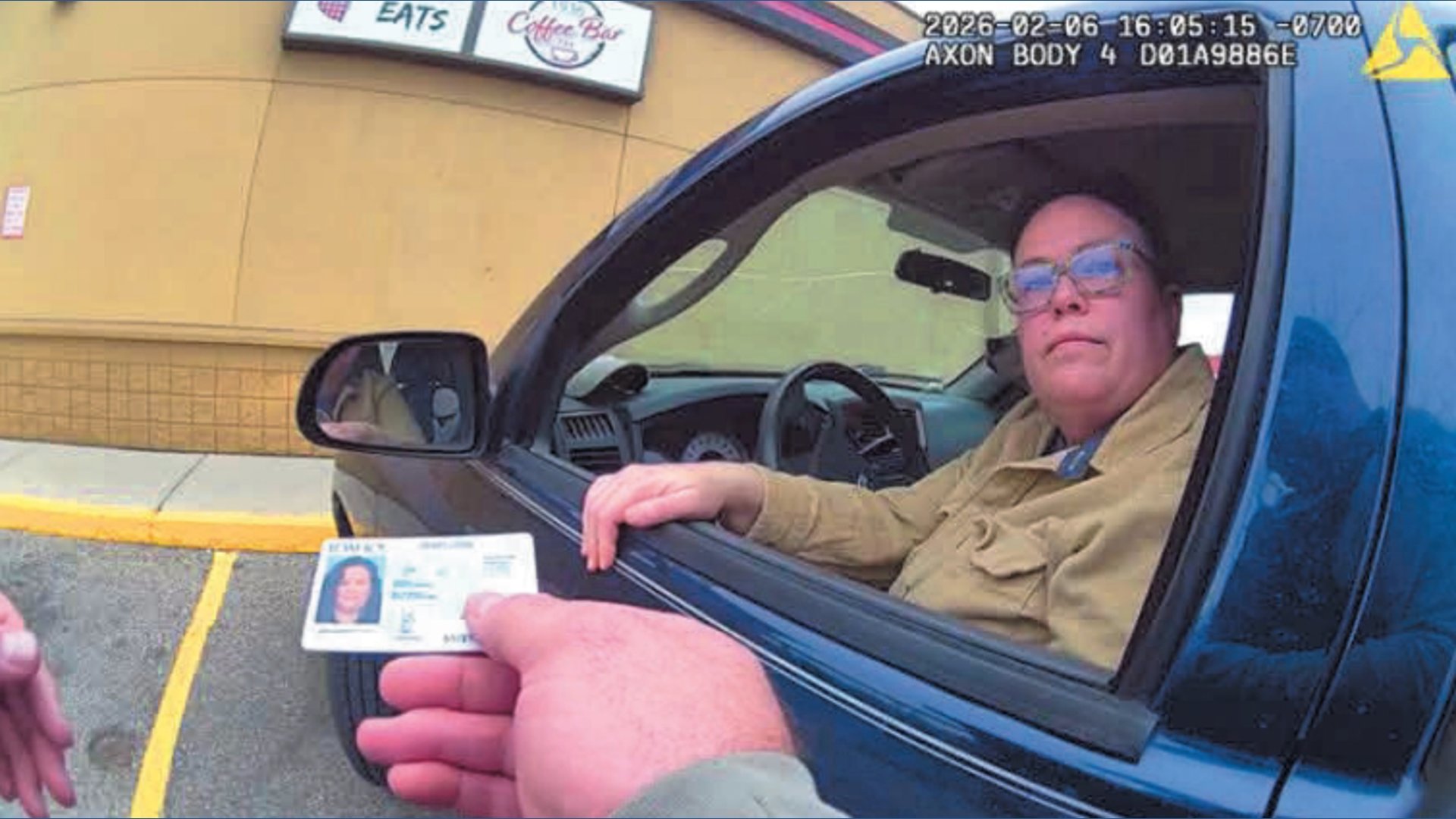A person in a vehicle hands over an ID to another individual during a traffic stop outside a coffee shop.