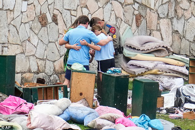 An officer prays with a family as they pick up items at Camp Mystic in Hunt, Texas, last July