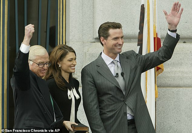 California Governor Gavin Newsom (right) waves during his swearing-in ceremony to become San Francisco mayor in January 2004 alongside his father, Judge William Newsom (left) and then wife Kimberly Guilfoyle (center)