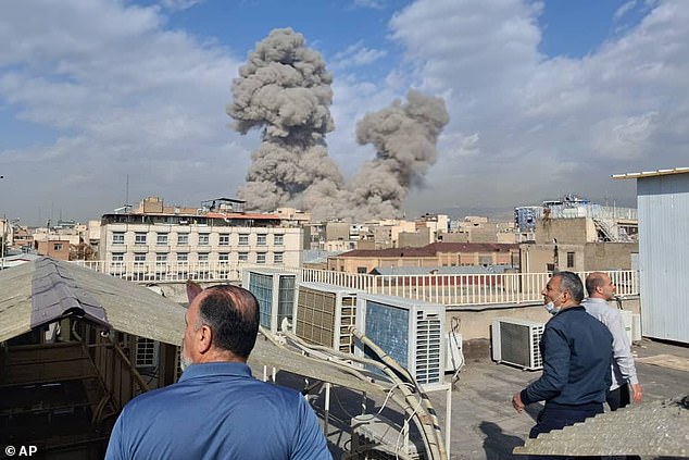 People watch as smoke rises on the skyline after an explosion in Tehran, Iran on Saturday