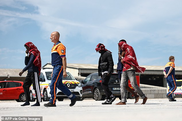 Migrants walk with a member of France's Civil Defence after disembarking from a French rescue ship following their rescue at sea after their boat caught fire during an attempt to cross the English Channel from France to Britain, at the Port de Commerce in Boulogne-sur-Mer, northern France, on August 4, 2026