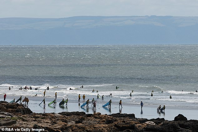 Surfers line the shore of the sea on Porthcrawl Rest Bay Beach in Bridgend, Wales