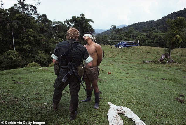A DEA agent stands with a blindfolded prisoner following the agency's raid on a cocaine lab in the Peruvian jungle