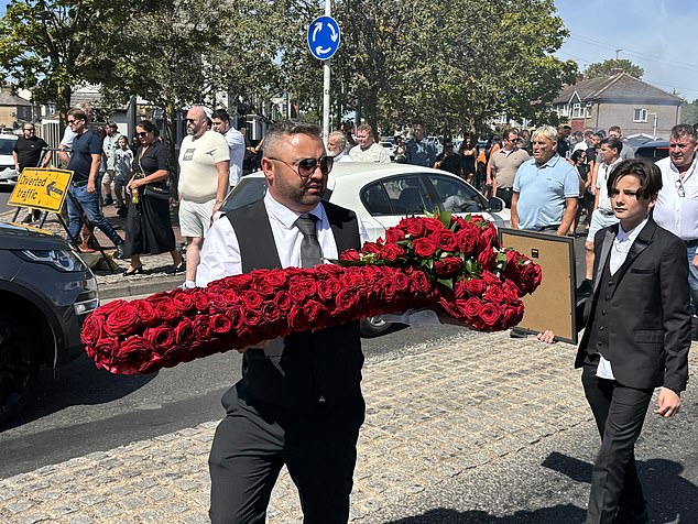 One man carries a floral tribute made up of red roses for Mr Hanrahan while another attendee carries a framed photo