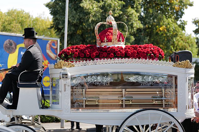 A carriage with a crown and bouquet of flowers is seen transporting the traveller's body during the service