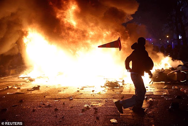 A man throws a plastic traffic cone through a burning barricade amid clashes
