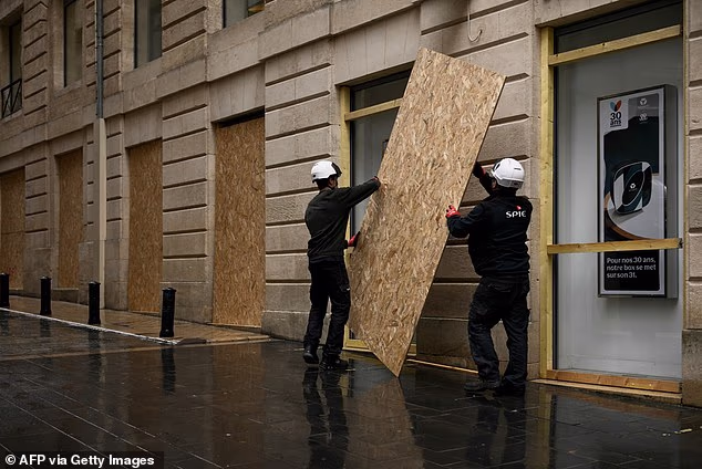 Workers lift a wooden panel to board up a shop window ahead of a demonstration planned in central Bordeaux, southwestern France