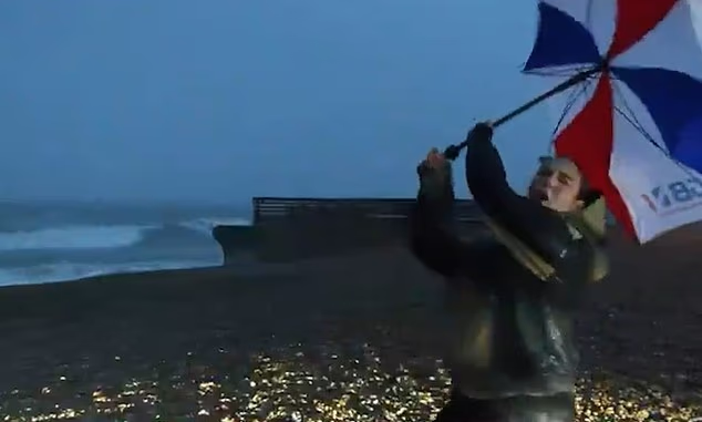 Moment umbrella-wielding TV news reporter is nearly blown away by Storm Austen as presenters are battered by 80mph winds