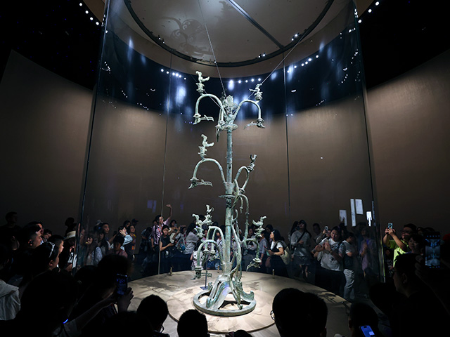Visitors view the Bronze Sacred Tree, one of the most renowned artifacts from the ancient Shu civilization, displayed at the Sanxingdui Museum on July 01, 2026 in Guanghan, China. The elaborately crafted bronze tree, dating back over 3,000 years, reflects the artistic and spiritual sophistication of the Sanxingdui culture. The Sanxingdui Museum received a total of 6.08 million visitors in 2025, nearly 200,000 visitors during the Spring Festival of 2026 (averaging nearly 30,000 visitors per day), and nearly 120,000 visitors during the five-day May Day holiday in 2026. The museum will extend its opening hours during the summer vacation of 2026. (Photo by Zhe Ji/Getty Images)