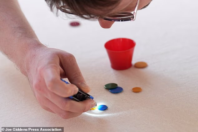 Umpire Harley Jones uses a torch to check whether 'winks' are touching during the 2026 World Singles Tiddlywinks Championship