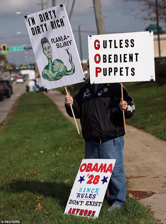An anti-Ramaswamy protester holds signs mocking the GOP gubernatorial candidate, including a cartoon depicting him as a snake