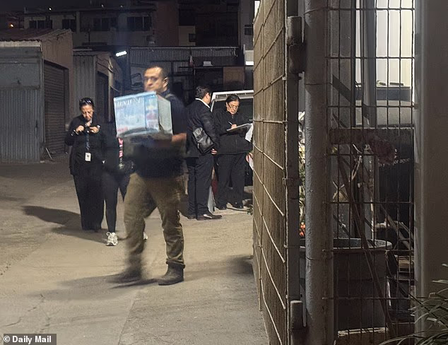 A grim-faced official with the Mexican Guardia Nacional totes a cardboard box during Saturday's raid at Thomas Markle's storage facility